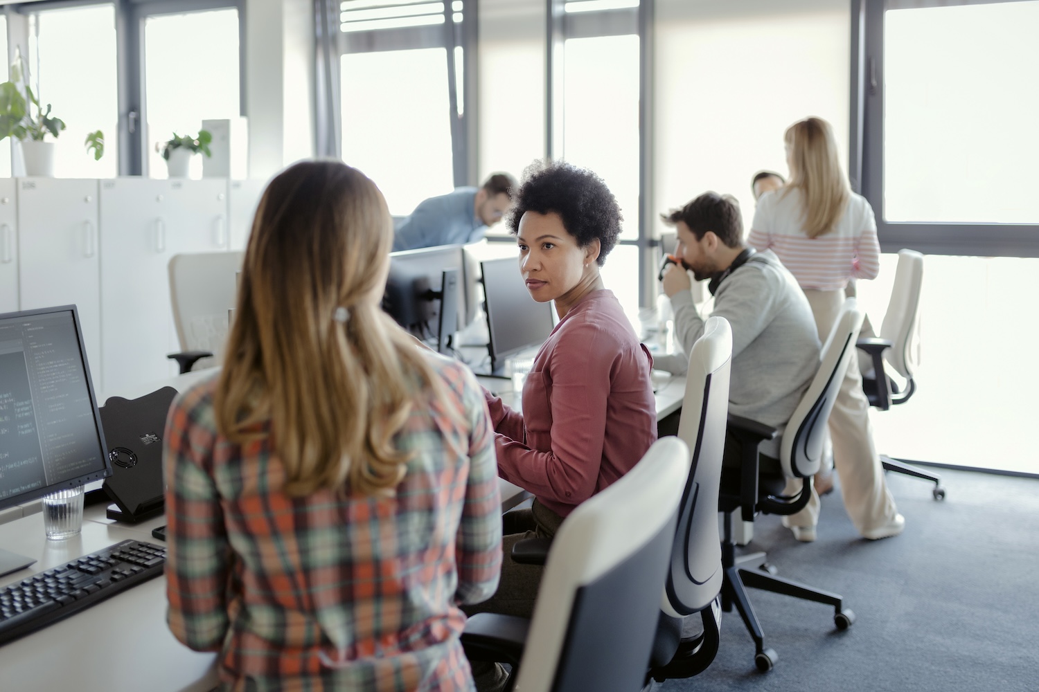 Several office employees holding a conversation in front of their computers