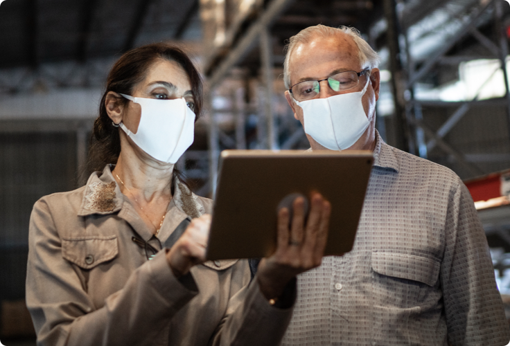 Two masked warehouse workers looking at an iPad screen