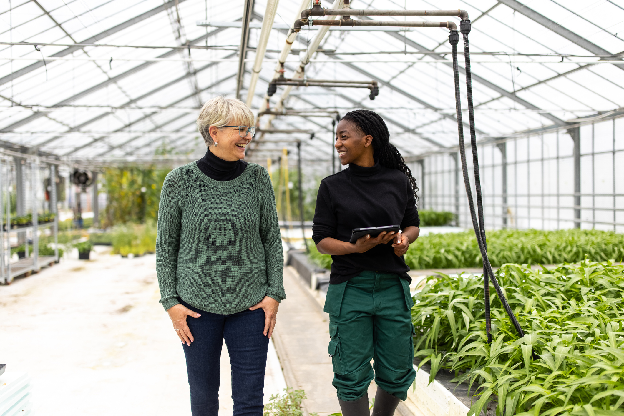 A younger and older woman walking through a greenhouse