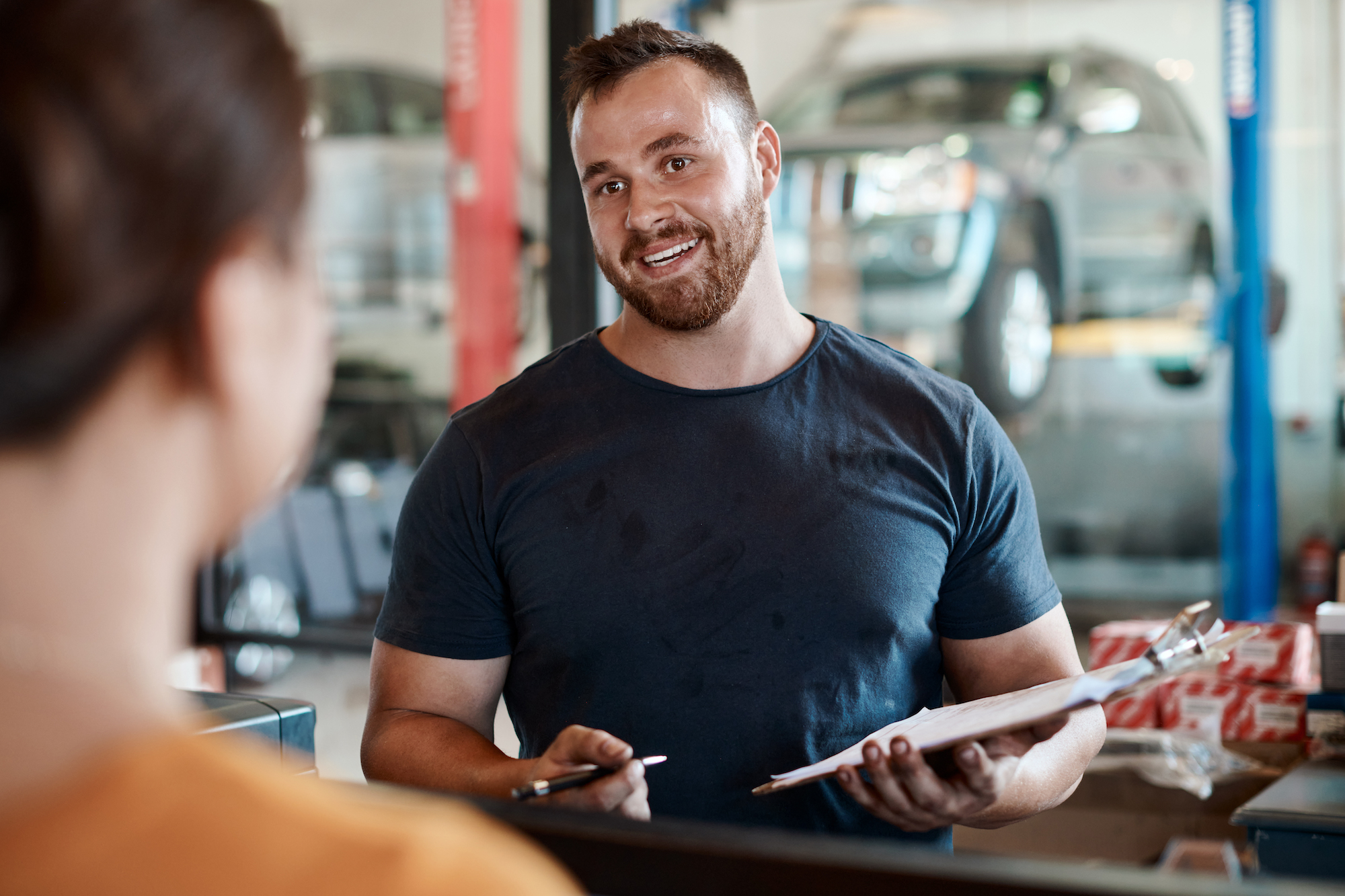 A mechanic holding a clipboard talking to a customer